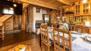 Una cocina rústica con armarios de madera, una chimenea de piedra y una zona de comedor con sillas y una mesa dispuesta para dos personas.