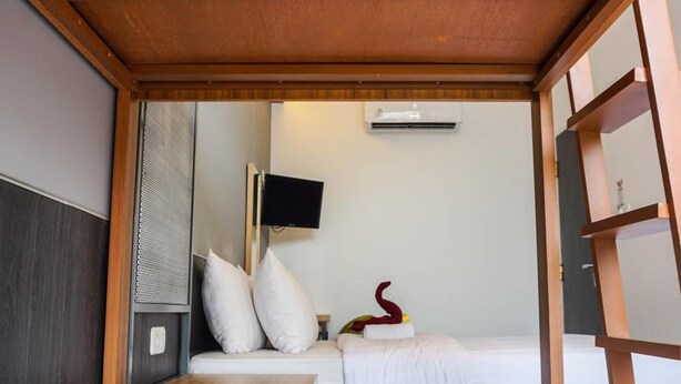 A compact hotel room with a wooden ceiling, a bed with white bedding, a small bedside table, a wall-mounted TV, and a decorative item on the nightstand. - Hotel Pantes Simpang Lima Semarang (Semarang)