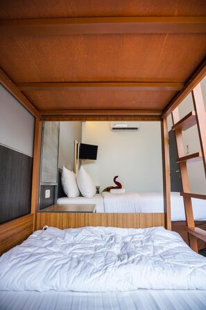 A compact hotel room with a wooden ceiling, a bed with white bedding, a small bedside table, a wall-mounted TV, and a decorative item on the nightstand. - Hotel Pantes Simpang Lima Semarang (Semarang)