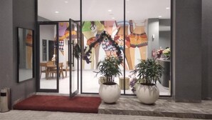 A hotel entrance with a glass door, a red carpet, and two large potted plants. - Hotel Pantes Simpang Lima Semarang (Semarang)