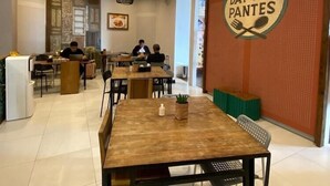 A modern dining area with wooden tables and chairs, a wall-mounted sign reading "Dapoer Pantes," and a seating area with a green bench. - Hotel Pantes Simpang Lima Semarang (Semarang)