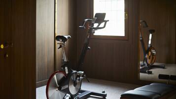 A room with a stationary bike, a bench, and a window with blinds.