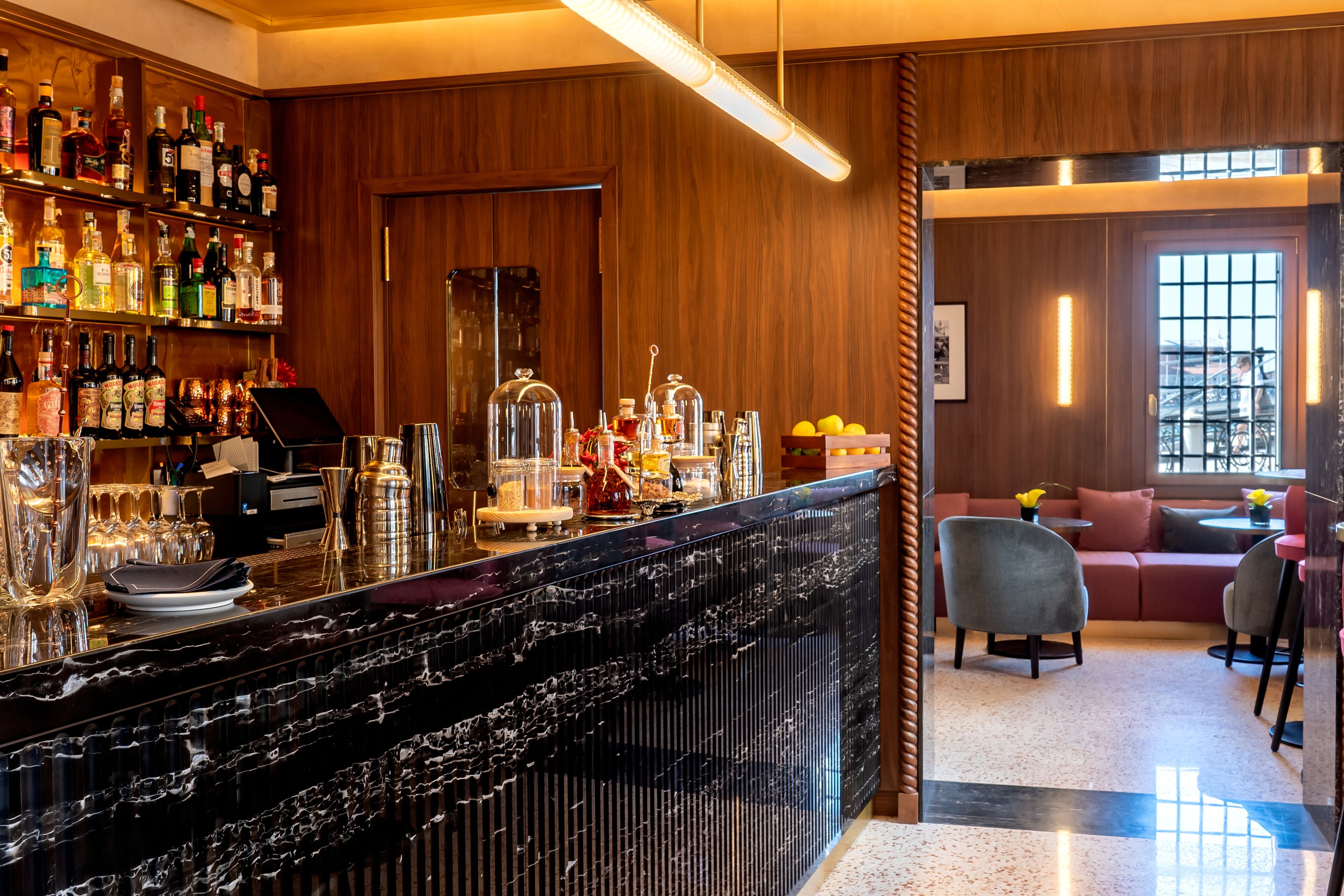 A bar area with a marble counter, shelves of liquor bottles, and a seating area with a sofa and chairs.