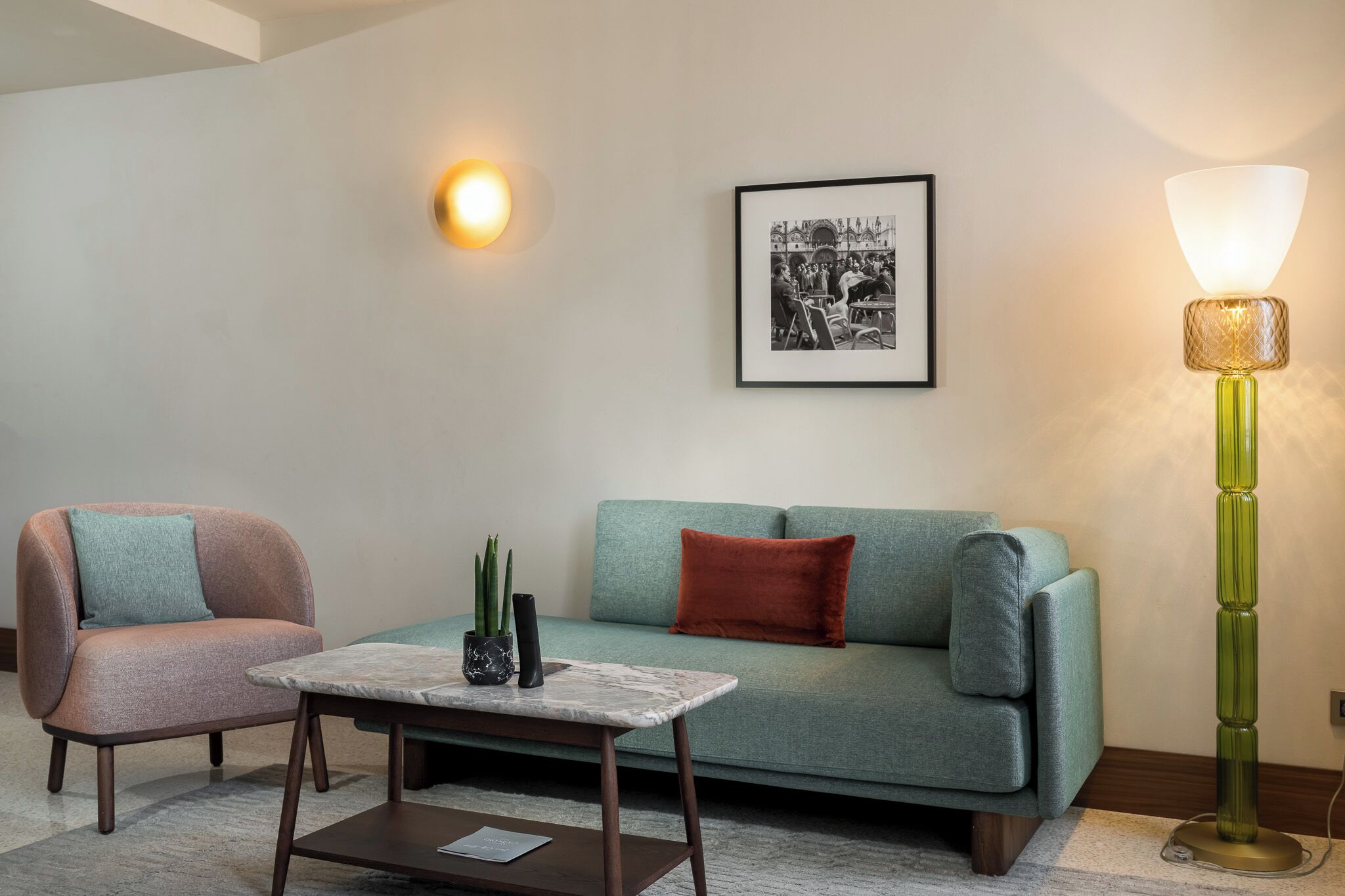 A living room with a sofa, two armchairs, a coffee table, a floor lamp, a wall-mounted light, and a framed picture.