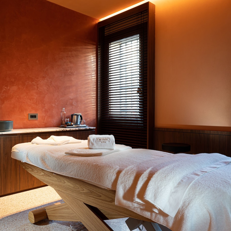 Un cuarto de spa con camilla de masaje, armarios de madera, un lavabo y una ventana con persianas.