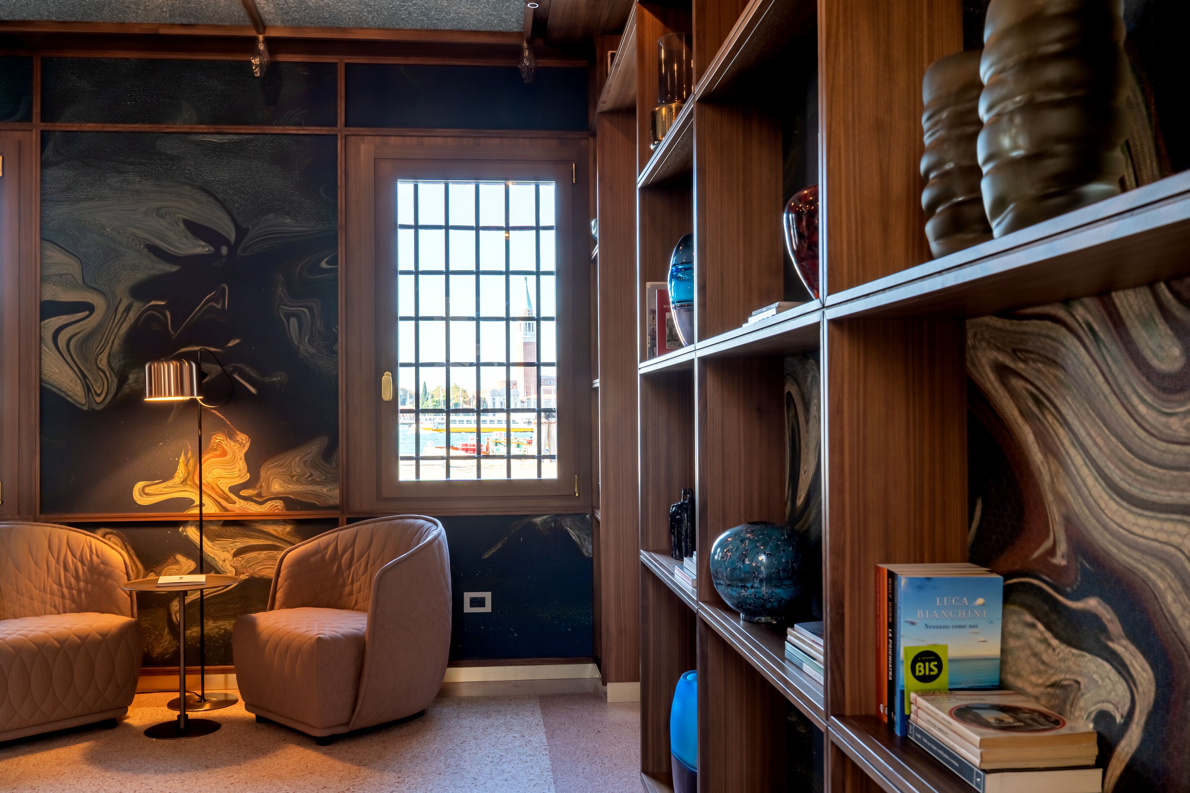 Une chambre moderne dotée d’une grande fenêtre, d’une bibliothèque et d’un coin salon avec une lampe.