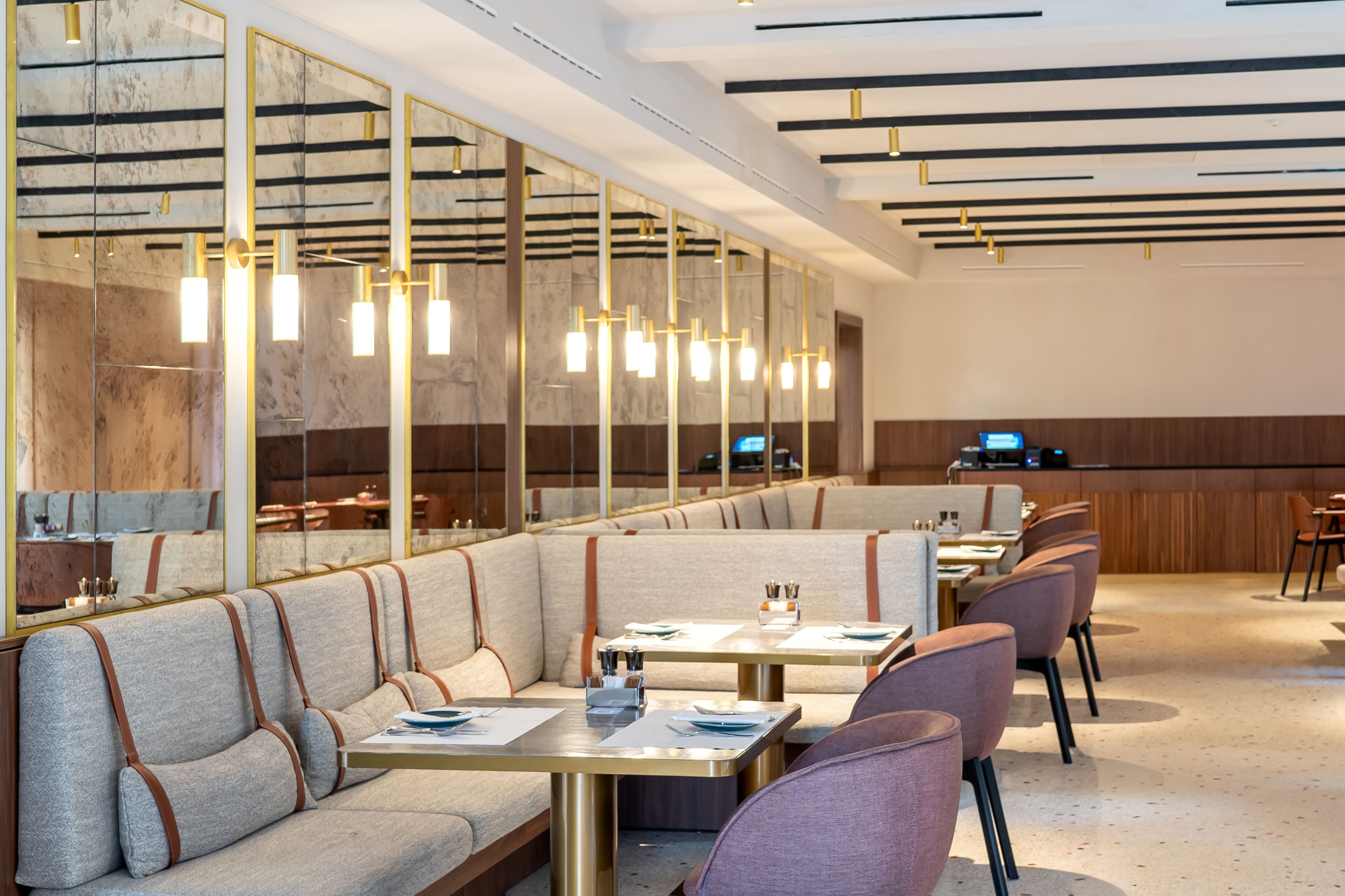 A modern restaurant with booth seating, long tables, and pendant lighting.