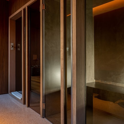 Habitación de hotel con piso de madera, puerta corredera de vidrio que da al baño y lavamanos de mármol.
