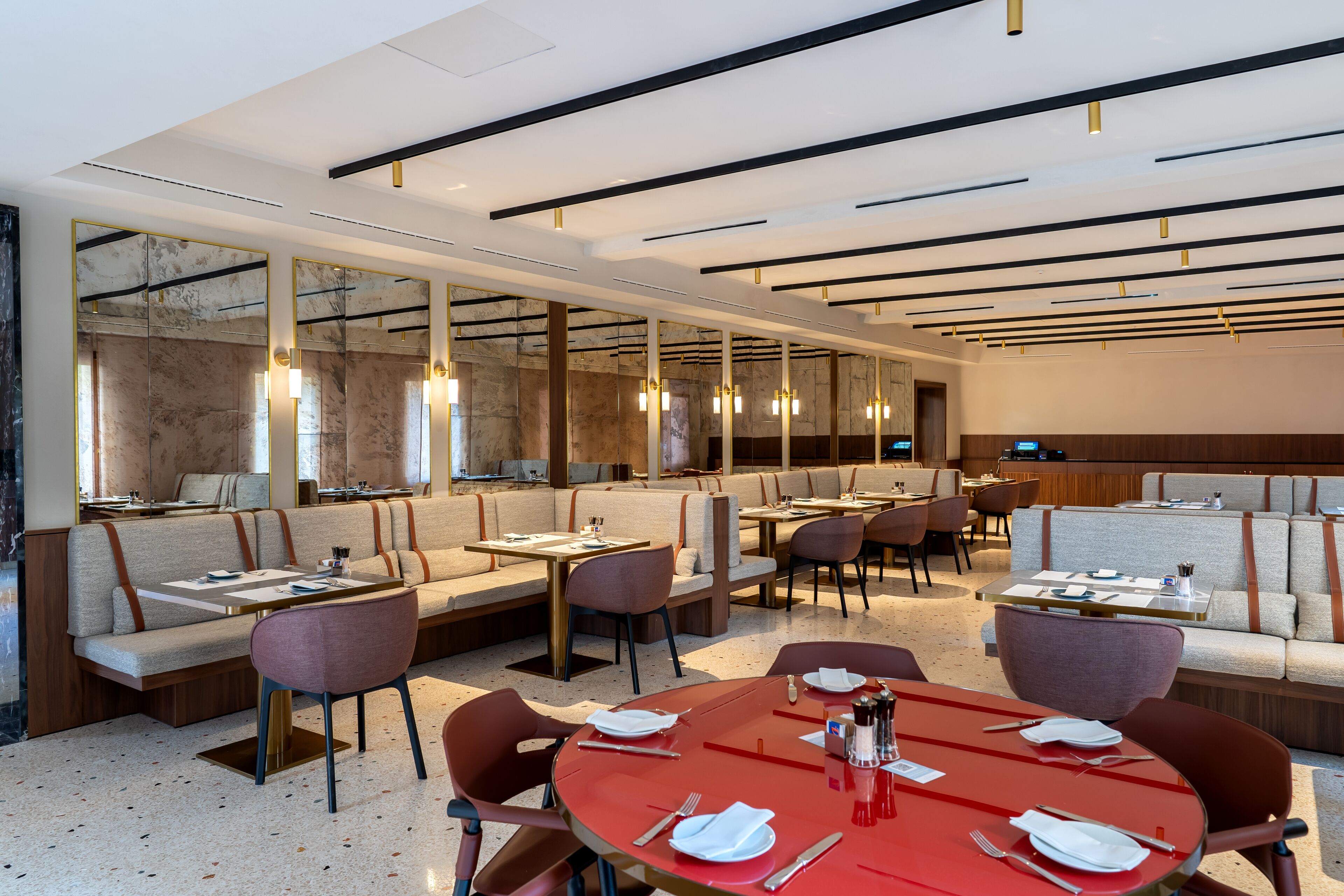 A modern restaurant with high ceilings, mirrored walls, and a mix of seating options including tables and sofas.