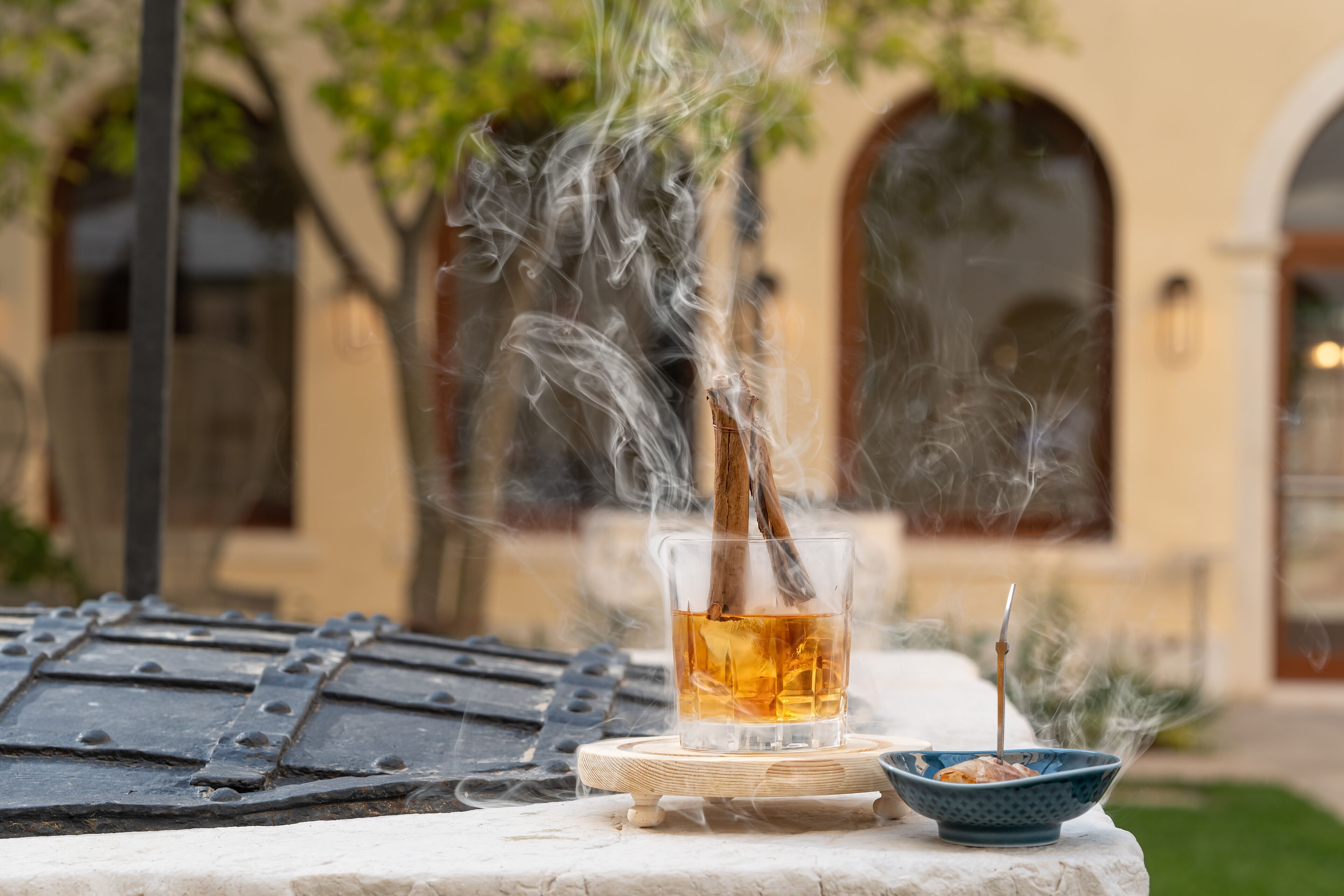 Un verre contenant un liquide ambré, posé sur un dessous de verre, un récipient avec une baguette, et de la fumée s'élevant d'un autre récipient.