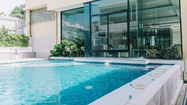 Un área de piscina moderna con agua azul cristalina, un jacuzzi integrado y un patio con paredes de vidrio.