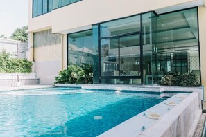 Ein moderner Poolbereich mit klarem, blauem Wasser, einer eingebauten Whirlwanne und einer verglasten Terrasse.