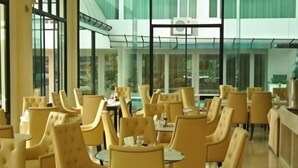Un espacio interior amplio con sillas y mesas tapizadas en amarillo, ventanas grandes y un diseño arquitectónico moderno.
