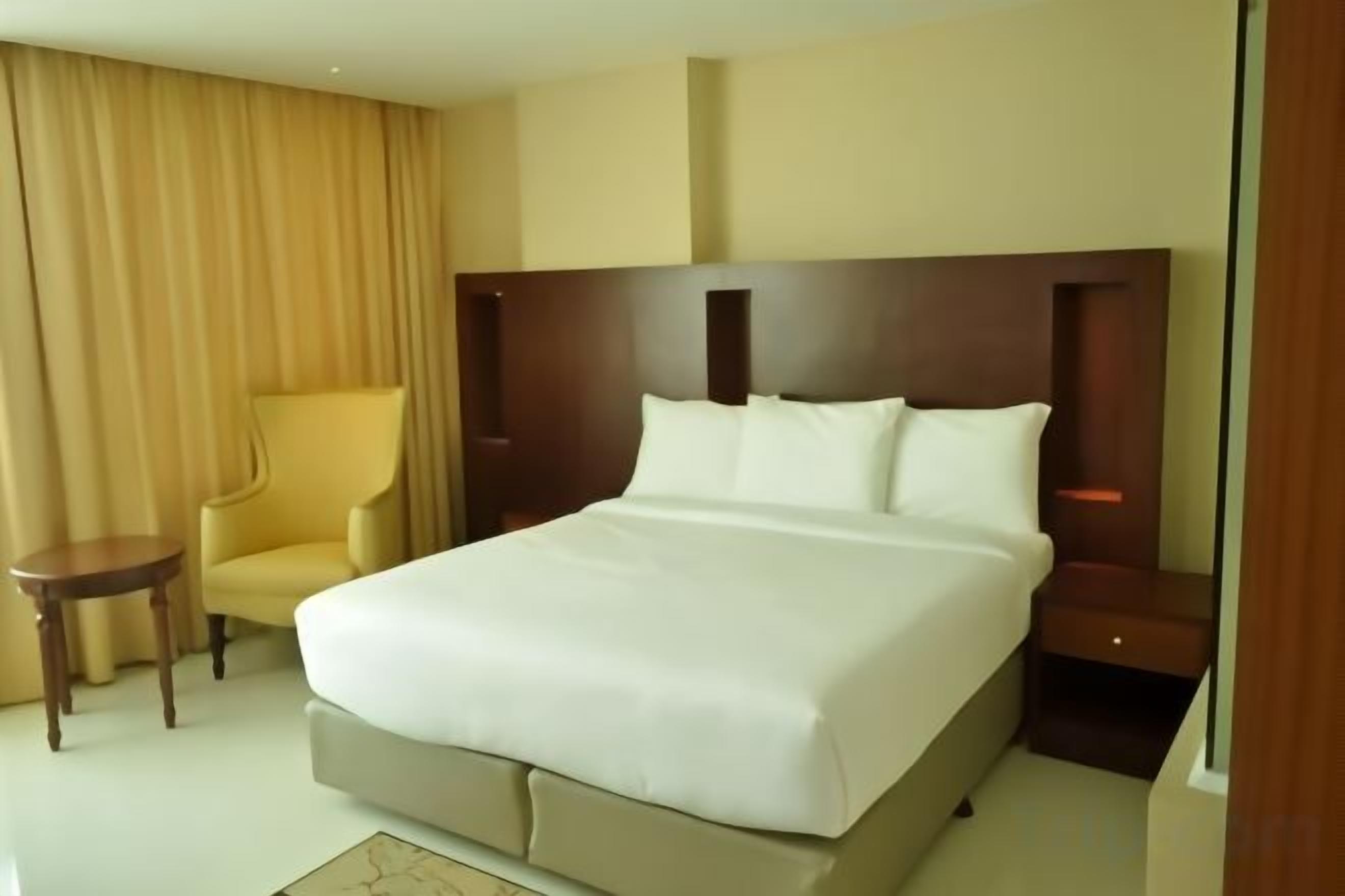 A hotel room with a large bed, a bedside table, a chair, and a curtain.