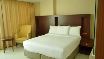 A hotel room with a large bed, a bedside table, a chair, and a curtain.