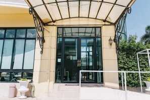 A hotel entrance with a covered entrance, large windows, and outdoor seating. - Aramis Hotel (Nakhon Sawan)