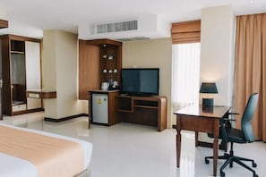 A hotel room with a bed, a desk with a chair, a television, a mini-fridge, and a wardrobe. - Aramis Hotel (Nakhon Sawan)
