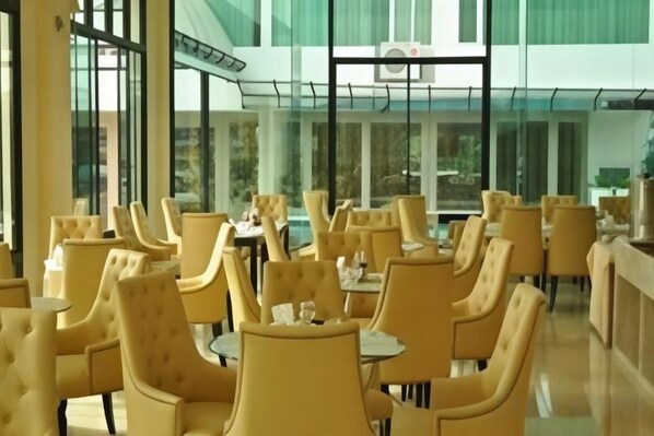 A spacious indoor dining area with high ceilings and large windows. Tables are arranged in a grid pattern, and there are numerous chairs around them. - Aramis Hotel (Nakhon Sawan)