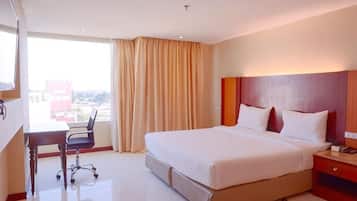 Ein Hotelzimmer mit einem großen Bett, einem Schreibtisch und Blick auf die Stadt.