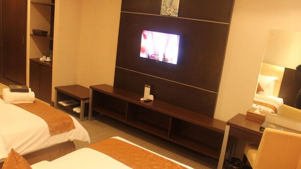 A hotel room with two beds, a TV on the wall, a desk with a chair, and a small table. - Royal Suite Hotel Balikpapan (Balikpapan)