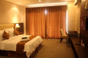 A hotel room with a large bed, a desk, a chair, and a TV.