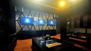 A room with a patterned wall, three screens displaying logos, a glass display table with items, and a wooden floor. - Royal Suite Hotel Balikpapan (Balikpapan)