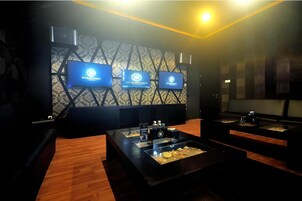 Una habitación con pared estampada, tres pantallas mostrando logotipos, una mesa expositora de vidrio con objetos y suelo de madera.