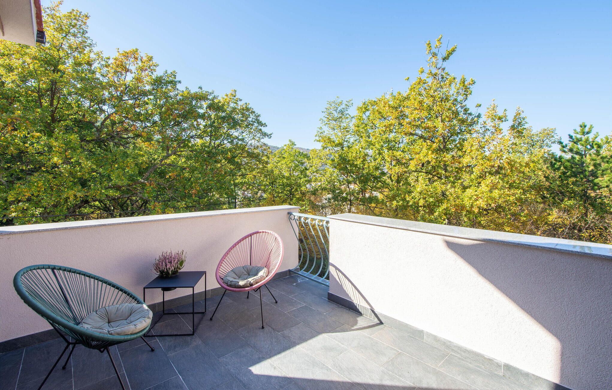 Ein Balkon mit zwei Korbstühlen, einem kleinen Tisch und einem Blumentopf.