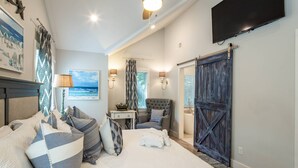 A bedroom with a bed, pillows, a nightstand, a chair, a TV, and a sliding door. - Family-Friendly; Steps to Beach; Fabulous Backyard w/ Screened Porch, Expansive Back Deck & Fire Pit (Isle of Palms)