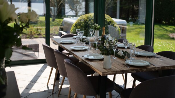 A dining table set for six with chairs, a bottle of champagne, and a view of a garden and lake. - MIL ROSES EN BAIE 9 PEOPLE NEAR MARQUENTERRE (SAINT QUENTIN EN TOURMONT)