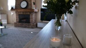 A wooden table with candles and a vase of flowers in a living room with a fireplace and a clock on the wall. - MIL ROSES EN BAIE 9 PEOPLE NEAR MARQUENTERRE (SAINT QUENTIN EN TOURMONT)