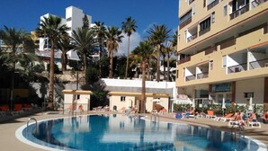 A swimming pool surrounded by palm trees and a multi-story building with balconies. - 211 Los Cristianos First Sea Line, Swimming pool (Los Cristianos)