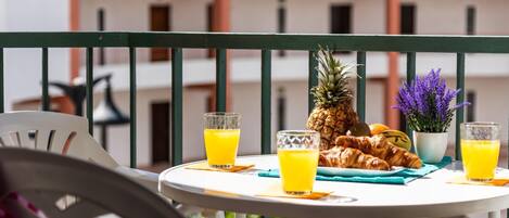 Ein Balkon mit einem Tisch, gedeckt für das Frühstück, darunter Croissants, eine Ananas und Gläser Orangensaft.
