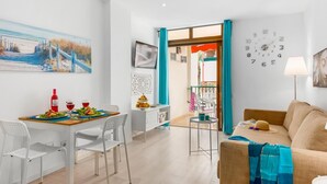A modern living room with a dining area, featuring a wooden table set for two, white chairs, a beige sofa, and a teal-colored throw over the sofa. - 211 Los Cristianos First Sea Line, Swimming pool (Los Cristianos)
