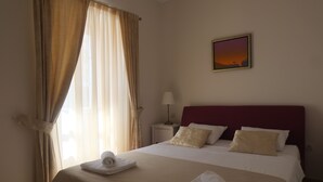 Een net opgemaakt bed met witte lakens en een rode hoofdbord, een bedlamp en een schilderij van een zonsondergang aan de muur.