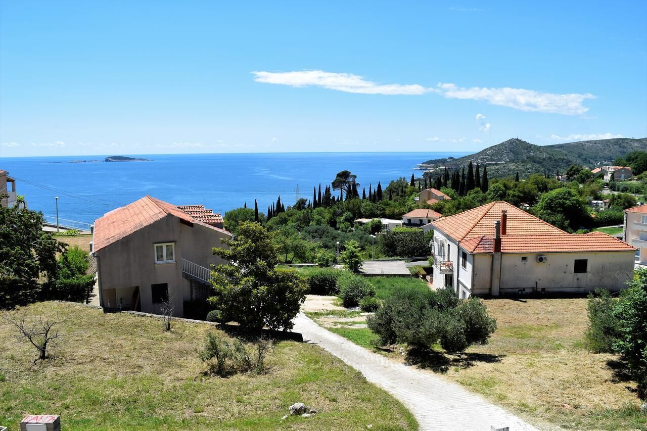 Ein Küstenwohngebiet mit Häusern, freiem Blick auf das Meer und einer hügeligen Landschaft im Hintergrund.