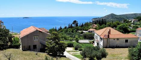 A coastal residential area with houses, a clear view of the sea, and a hilly landscape in the background.