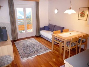 A cozy living room with a sofa, a dining table with chairs, a rug, and a television.