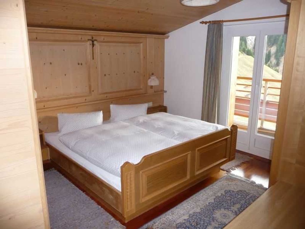 A bedroom with a wooden bed, a large window, and a view of the outdoors.