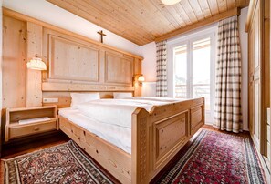 A wooden bedroom with a bed, nightstands, and a window with curtains. - Gamsljager - Appartementhaus Rotwandblick (Faschina)