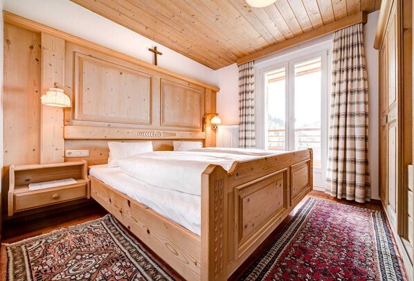 A wooden bedroom with a bed, nightstands, and a window with curtains.