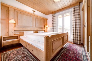 A wooden bedroom with a bed, nightstands, and a window with curtains.