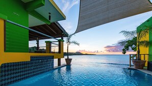 Ein Poolbereich mit Blick auf den Ozean, eine überdachte Lounge und ein Gebäude mit grünen und gelben Wänden.