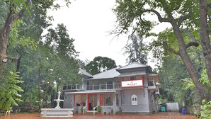 A two-story building with a signboard, a fountain, and a paved courtyard surrounded by trees. - Ritz Heritage (Mawal)