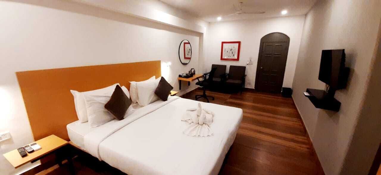 A hotel room with a bed, a nightstand, a desk, a chair, a TV, and a door.