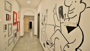 A hallway with framed artwork on the walls, a large cartoon mural, and a door at the end. - Ritz Heritage (Mawal)