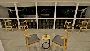 A terrace with six wooden chairs and a small round table, surrounded by large windows. - Ritz Heritage (Mawal)