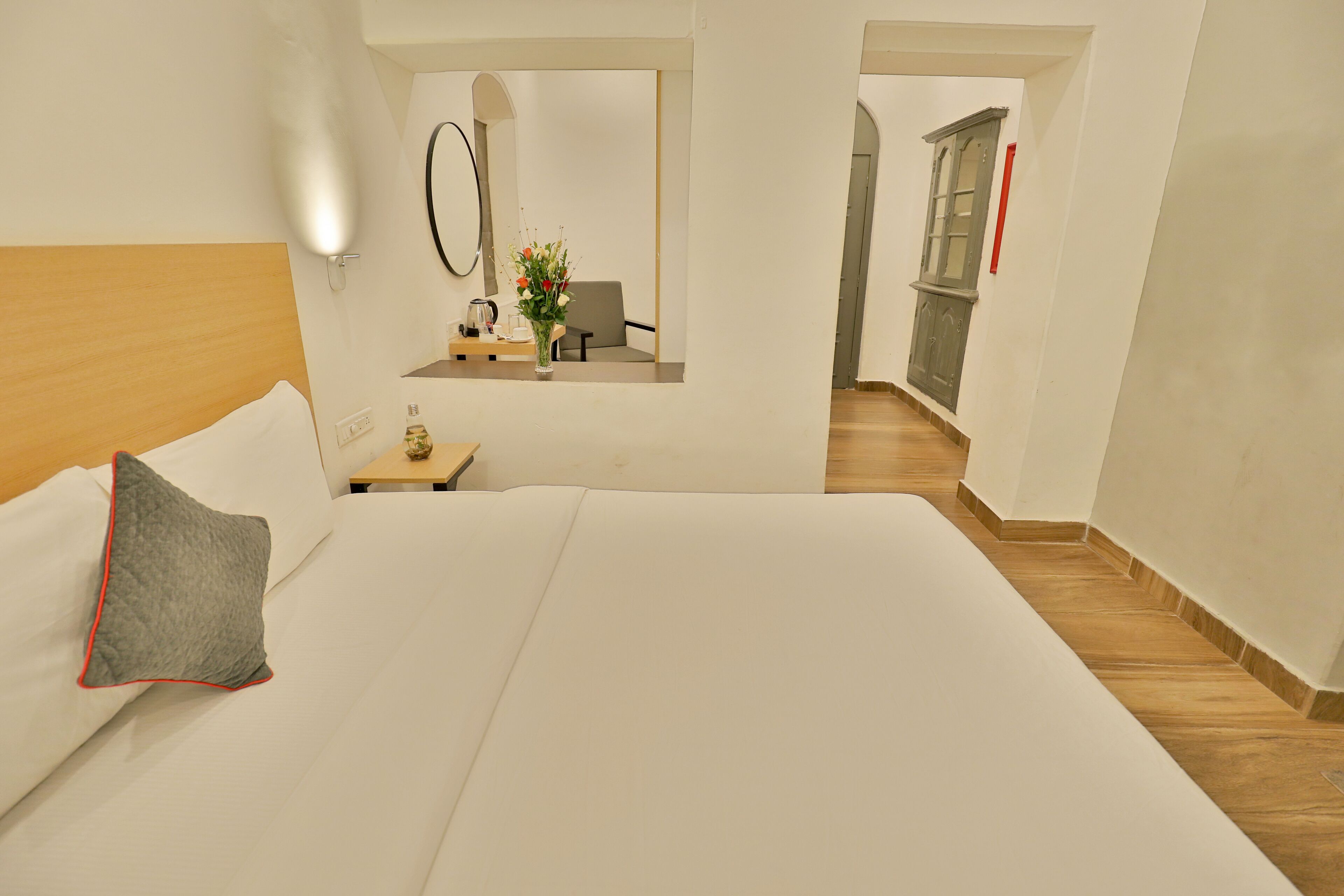 A hotel room with a large bed, a bedside table with a vase of flowers, a mirror, and a view of a hallway.
