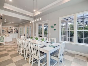 A dining area with a checkered floor, white chairs, a white table set for four, and large windows with a view of greenery.