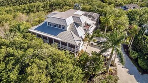 Una casa gran envoltada de vegetació tropical densa, amb vistes a una massa d'aigua i una petita illa a la distància.